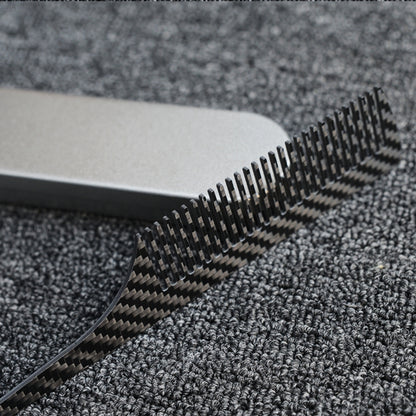 Close-up of a carbon fiber comb with a distinct woven pattern, placed next to a silver metal case on a dark gray textured fabric surface.