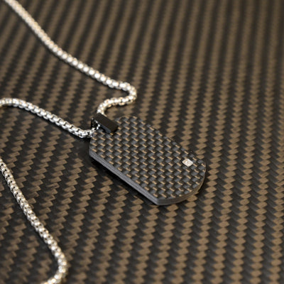 Close-up of a 3K carbon fiber oval pendant with a checkered pattern and a small diamond accent, paired with a silver-tone chain