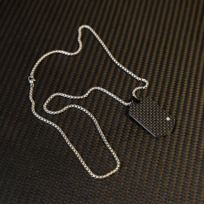 Close-up of a 3K carbon fiber dog tag pendant with a checkered pattern and a small diamond accent, paired with a silver-tone chain