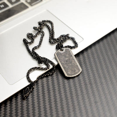 Close-up of a 3K carbon fiber dog tag pendant with metallic detailing, paired with a black-toned chain