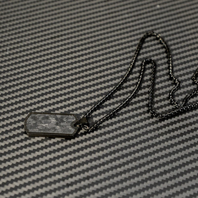 Close-up of a 3K carbon fiber dog tag pendant with a textured surface, paired with a black-toned chain