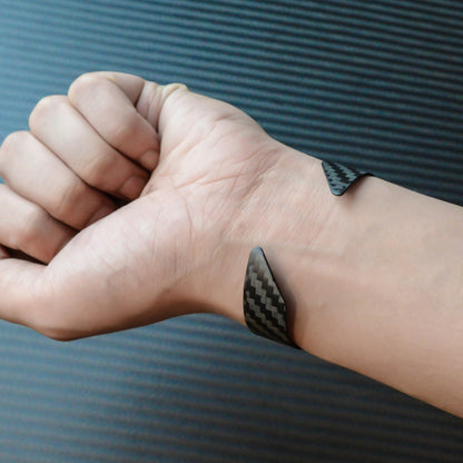 A 3K carbon fiber cuff bracelet with a distinct weave pattern, worn on a wrist against a background with carbon fiber texture.