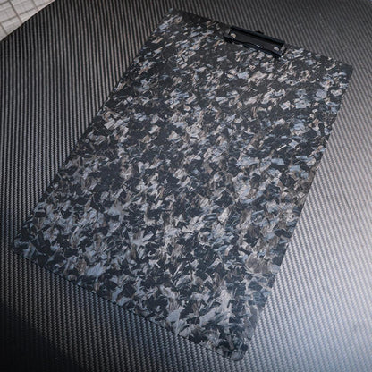 Close-up detail of a forged carbon fiber clipboard with a marbled pattern, featuring a black clip, placed on a carbon fiber-textured surface.