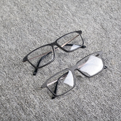 Close-up of two eyeglass frames made from forged carbon fiber and 3K carbon fiber, featuring sleek black designs with clear lenses, placed on a textured gray surface.
