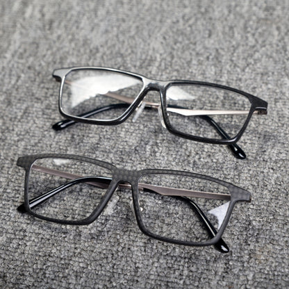 Close-up of two eyeglass frames featuring forged carbon fiber and 3K carbon fiber constructions, with sleek black designs and clear lenses, placed on a textured gray surface.