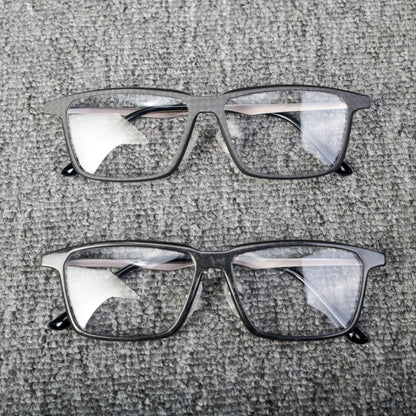 Close-up of two pairs of eyeglass frames crafted from forged carbon fiber and 3K carbon fiber, showcasing sleek black designs with clear lenses, placed on a textured gray surface.