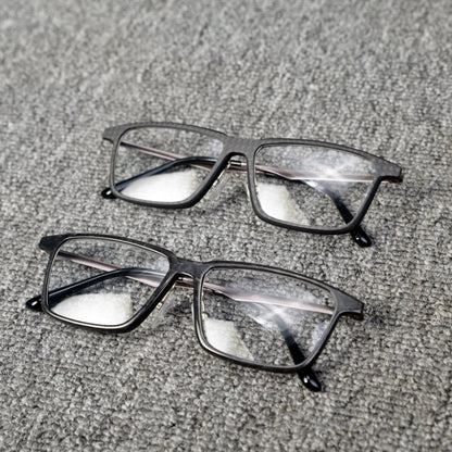 Close-up of two pairs of eyeglass frames crafted from forged carbon fiber and 3K carbon fiber, showcasing sleek black designs with clear lenses, placed on a textured gray surface.