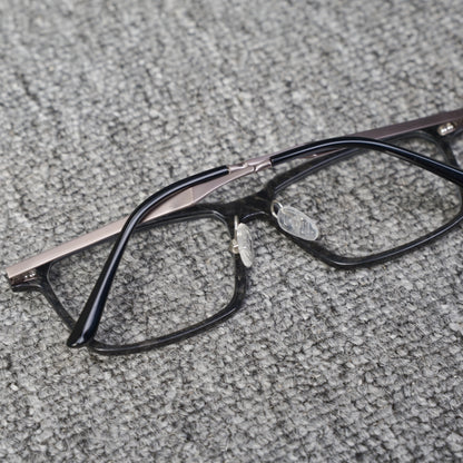 Close-up reverse side detail of a forged carbon fiber eyeglass frame, featuring clear nose pads and black with metallic temples, placed on a textured gray surface.