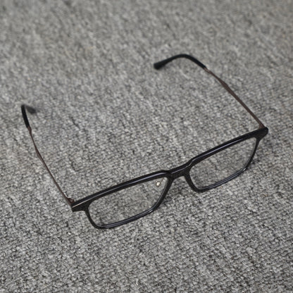 Close-up top detail of a forged carbon fiber eyeglass frame with a sleek black rectangular design, placed on a textured gray surface.