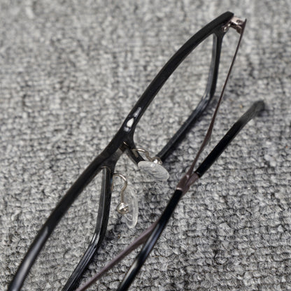 Close-up top detail of a forged carbon fiber eyeglass frame with a sleek black design, clear nose pads, and metallic components, placed on a textured gray surface.