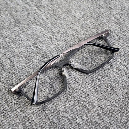 Close-up reverse side detail of a 3K carbon fiber eyeglass frame with a sleek black textured pattern and metallic temples, placed on a textured gray surface.