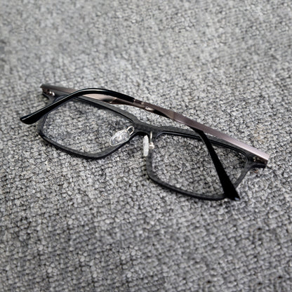 Close-up reverse side detail of a 3K carbon fiber eyeglass frame, showcasing its sleek black textured pattern and metallic temples, placed on a textured gray surface.