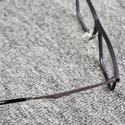 Close-up side detail of a 3K carbon fiber eyeglass frame, featuring a sleek black design and metallic temple, placed on a textured gray surface.