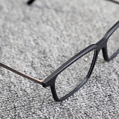 Close-up side detail of a 3K carbon fiber eyeglass frame, highlighting its sleek black carbon fiber pattern and metallic temple