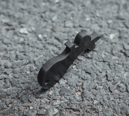 Close-up of a rabbit-shaped 3K carbon fiber keychain with a sleek black finish, placed on a rough asphalt surface.