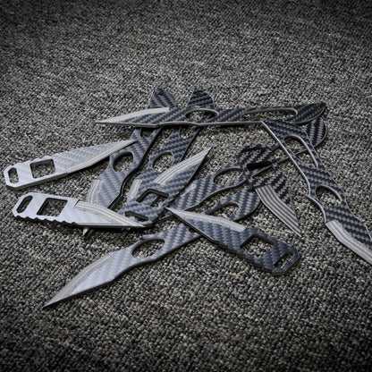 Close-up of multiple carbon fiber knives with various designs, showcasing their sleek carbon fiber patterns, arranged on a dark gray textured fabric surface.