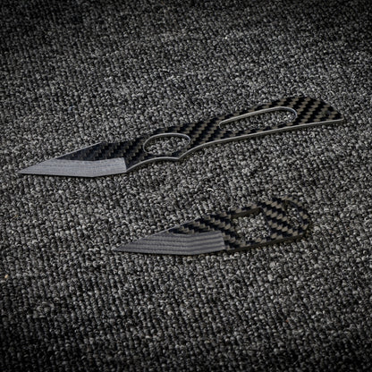Close-up of two carbon fiber knives with distinctive patterned handles and blades, displayed on a dark textured fabric surface.