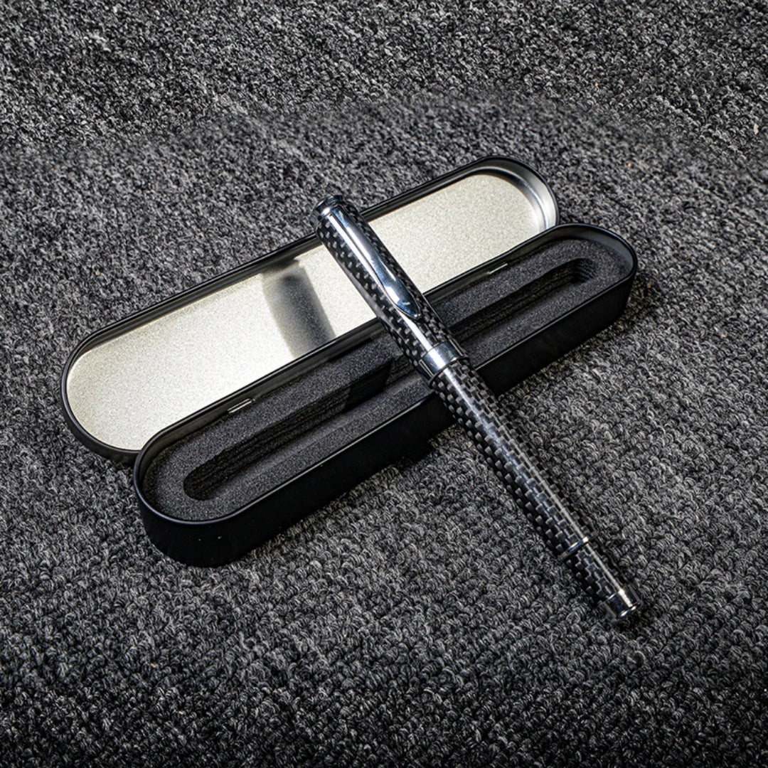 Close-up of a carbon fiber ballpoint pen with a distinct woven texture, paired with a black metal case featuring foam lining, displayed on a gray textured fabric surface.