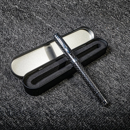 Close-up of a carbon fiber ballpoint pen with a distinct woven texture, paired with a black metal case featuring foam lining, displayed on a gray textured fabric surface.
