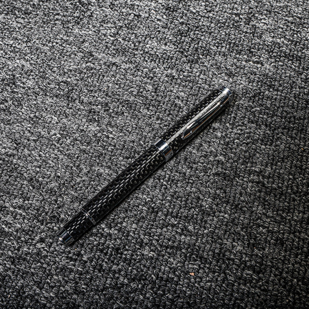 Close-up of a carbon fiber ballpoint pen with a distinct woven texture, displayed on a gray textured fabric surface.