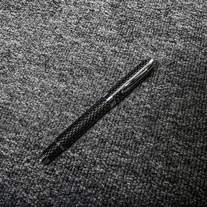 Close-up of a carbon fiber ballpoint pen with a distinct woven texture, displayed on a gray textured fabric surface.