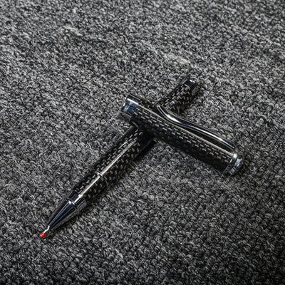 Close-up of a carbon fiber ballpoint pen with a distinct woven texture and metallic accents, displayed with its cap on a gray textured fabric surface.