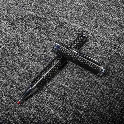 Close-up of a carbon fiber ballpoint pen with a distinct woven texture and metallic accents, displayed with its cap on a gray textured fabric surface.