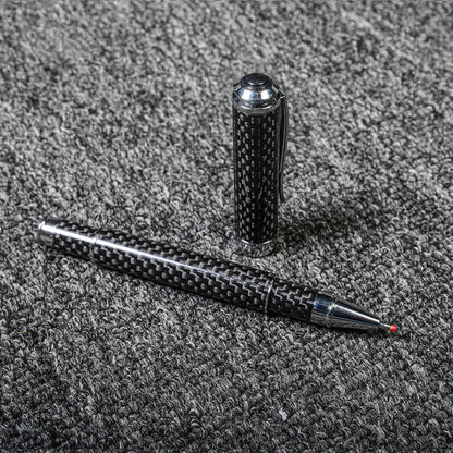 Close-up of a carbon fiber ballpoint pen with a distinct woven texture and metallic accents, displayed with its cap on a gray textured fabric surface.