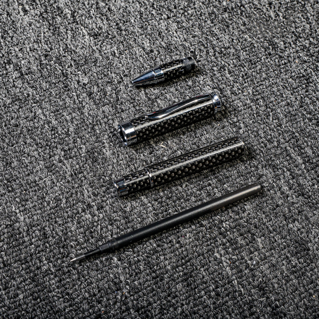 Close-up of a carbon fiber ballpoint pen disassembled into its components, showcasing the distinct woven texture and metallic accents, displayed on a gray textured fabric surface.