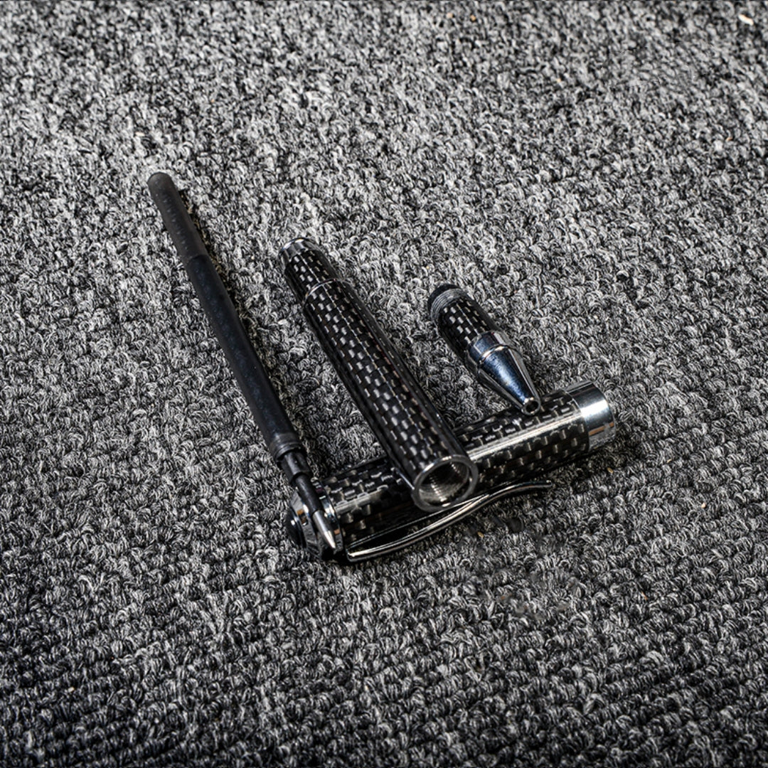 Close-up of a disassembled carbon fiber ballpoint pen with distinct woven texture and metallic accents, displayed on a gray textured fabric surface.