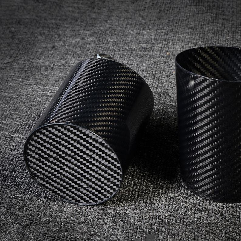 Two carbon fiber pen holders with distinct woven patterns, displayed on a gray textured surface.
