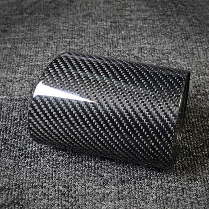 Close-up of a carbon fiber pen holder with a distinct woven pattern, laid on a gray textured fabric surface.