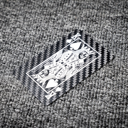 Close-up of a carbon fiber playing card featuring the King of Spades with white detailing, showcasing the distinct carbon fiber texture, laid on a gray textured surface.