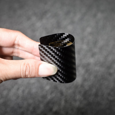 Close-up of a carbon fiber playing card with gold detailing, bent to showcase its flexibility, held by a hand