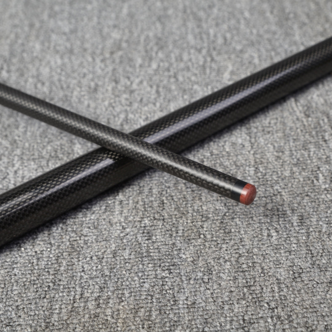 Two carbon fiber pool cue sections crossed over each other, featuring a textured carbon fiber finish with one section having a wooden tip, placed on a gray textured surface.
