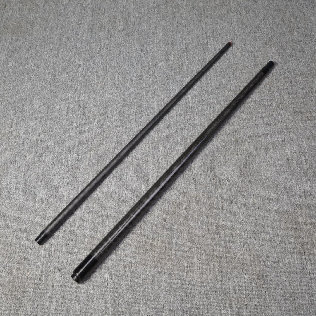 Two-piece carbon fiber pool cue laid out on a gray textured surface.