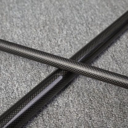 Close-up detail of a two-piece carbon fiber pool cue with a textured carbon fiber pattern, crossed on a gray textured surface.