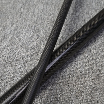 Close-up detail of two crossed sections of a carbon fiber pool cue, showcasing the textured carbon fiber pattern, placed on a gray fabric surface.