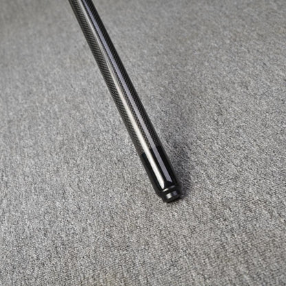 Close-up detail of the end of a carbon fiber pool cue, showcasing a textured carbon fiber pattern and a smooth black finish at the tip, placed on a gray textured surface.