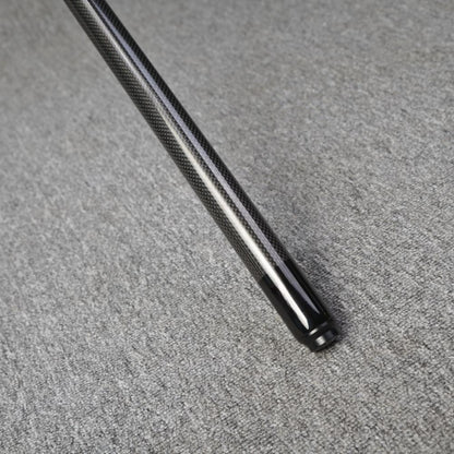 Close-up detail of the end of a carbon fiber pool cue, showcasing a smooth black finish at the tip and a textured carbon fiber pattern on the shaft, resting on a gray textured surface.