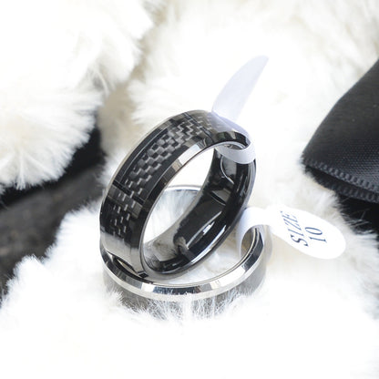 "Black ring featuring 3K carbon fiber detailing, paired with a size tag marked 'SIZE 10', resting on a soft, fuzzy texture."