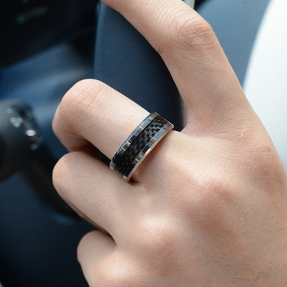 A hand wearing a ring with 3K carbon fiber detailing, set against a car interior background.