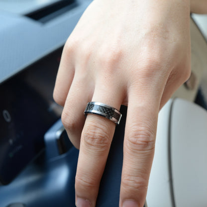 A hand wearing a ring with 3K carbon fiber detailing, set against a car interior background.
