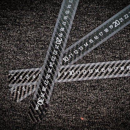 Three carbon fiber rulers with clear measurement markings, placed on a textured dark surface.