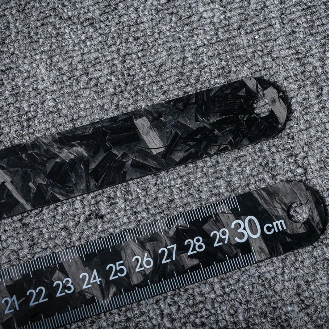 Two forged carbon fiber rulers displaying front and back sides with clear measurement markings, placed on a textured fabric background.