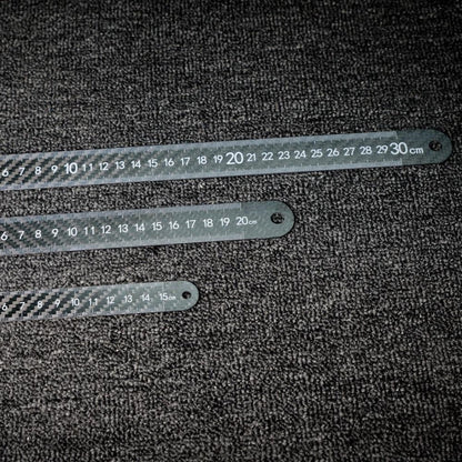 Three 3K carbon fiber rulers with distinct lengths and clear measurement markings, placed on a dark textured surface.