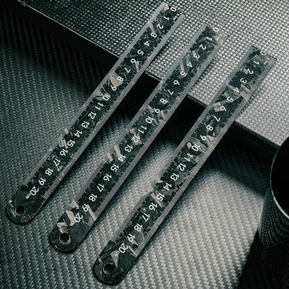 Three forged carbon fiber rulers with distinct patterns and clear measurement markings up to 20 cm, arranged on a carbon fiber textured surface.
