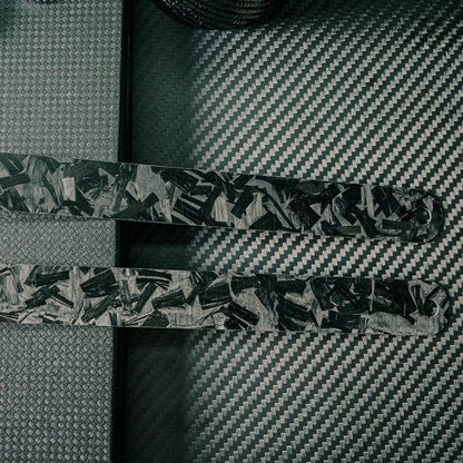 Close-up of the back sides of two forged carbon fiber rulers with distinct patterns, placed on a carbon fiber textured surface.