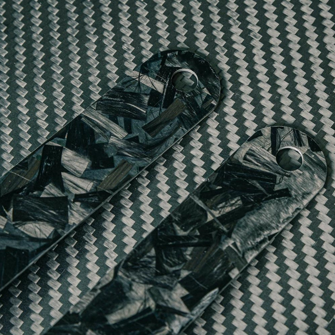 Close-up of the back sides of two forged carbon fiber rulers with distinct patterns, placed on a carbon fiber textured surface.