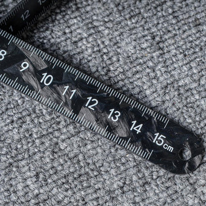 Close-up of a forged carbon fiber ruler with distinct patterns and clear measurement markings up to 15 cm, placed on a textured surface.